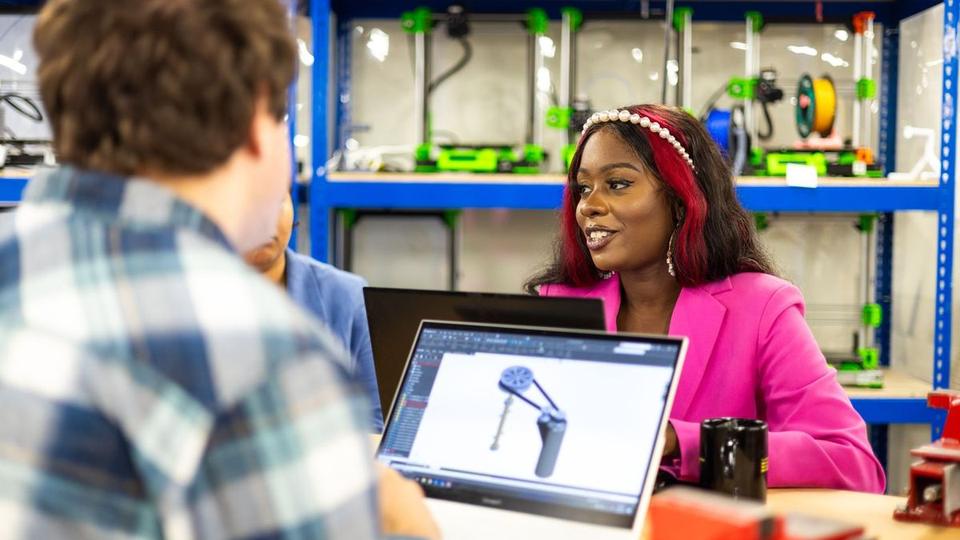 People talking in a workshop lined with 3D printers