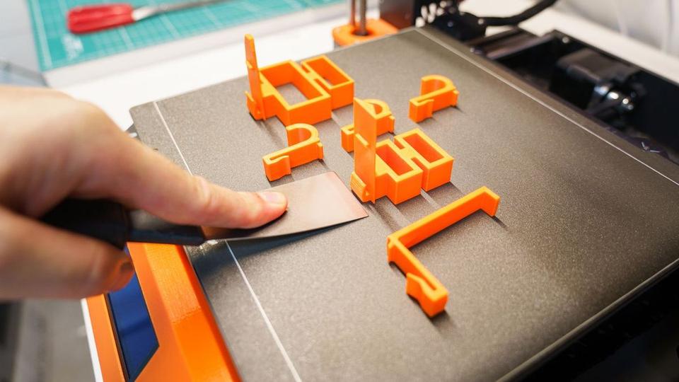 Hand lifting orange printed parts off a 3D printer bed